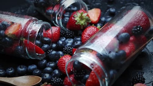 Cuisson de la confiture de framboises et de myrtilles. Déposer dans un bocal en verre. Rotation sur fond noir