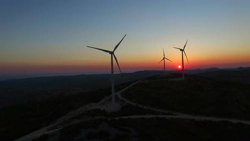 Luftaufnahme von langsam rotierenden Windmühlenblättern bei farbenfrohem Sonnenuntergang