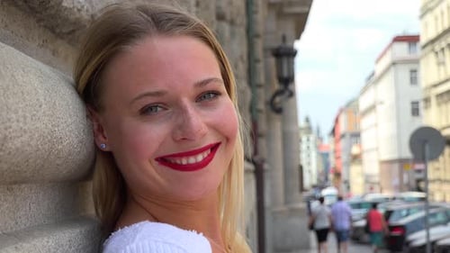A Young Beautiful Woman Leans Against a Wall in an Urban Area and Smiles at Camera - Face Closeup
