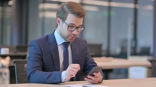 Excited Businessman Looking at Smartphone in Modern Office