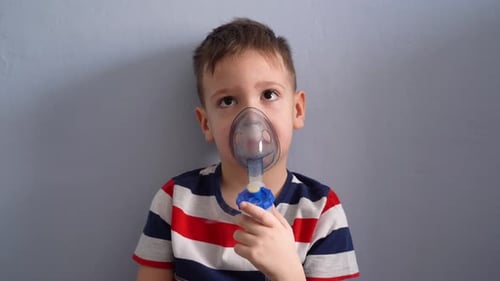 Child sitting on the bed takes a breath with a nebulizer