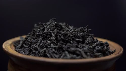 Close up view dry black ceylon tea leaves rotate in a clay bowl on black background