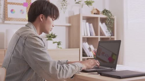 Young Adult Types on Laptop in Bright Office