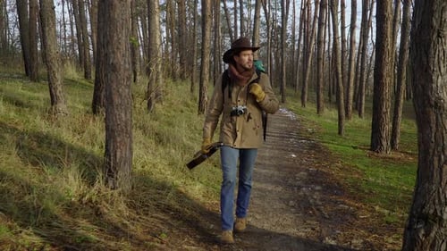 A Backpacker with a Guitar and a Camera Walks Along a Trail in the Forest