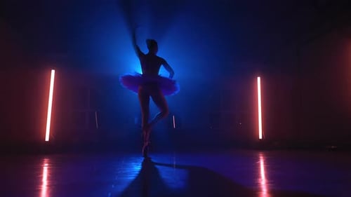 Sensual bailarina de ballet dando vueltas en un estudio oscuro con una luz de neón multicolor