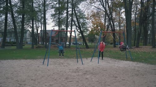 Happy Boy and Girl is Swaying on Swing in Park at Autumn Day and Jumping Out in Slow Motion.