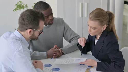 Young Businesswoman Discussing Reports with Colleagues While Sitting in Office