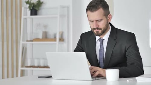 Stressed Businessman Working at Computer Touching Head
