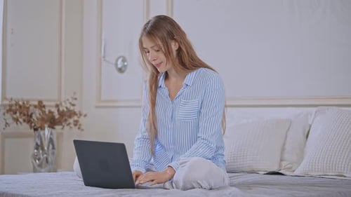 Woman Using Laptop on Bed in Pajamas