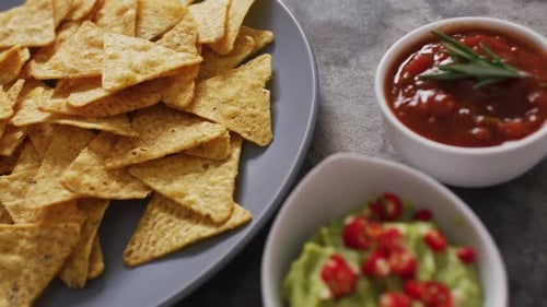 Primer plano de nachos en un plato y salsas sobre una superficie negra