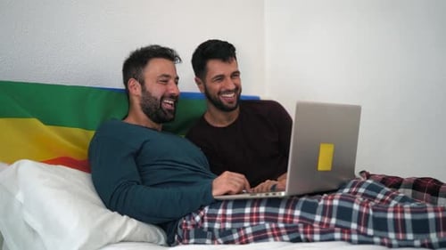 Couple Laughing in Bed Looking at Laptop