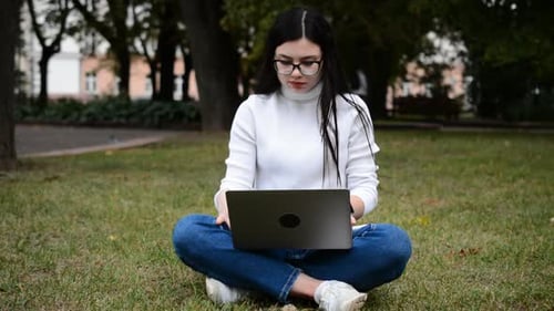 Caucasian College Girl Busy Using Laptop in the Lawn in Campus