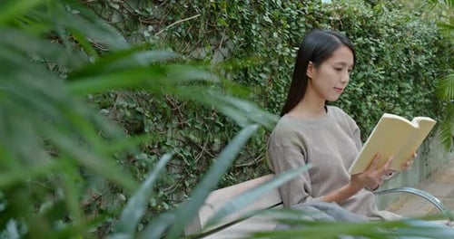 Young Woman Reading Book on Bench in Garden