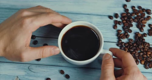 Hands holding steaming black coffee, overhead shot