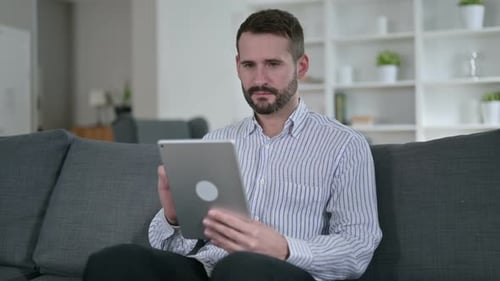 Man Celebrates Good News on Tablet at Home