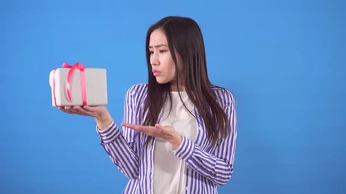 Dissatisfied with a Small Gift Young Sian Woman on a Blue Background