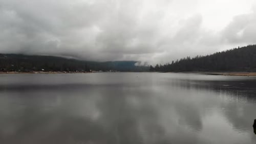 reverse aerial shot over lake revealing shoreline on a cloudy rainy day.