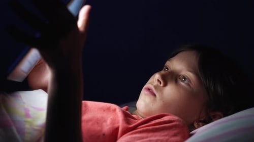 Petite fille allongée dans son lit et utilisant une tablette la nuit