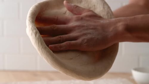Hands Stretching Dough in Bright Kitchen Environment