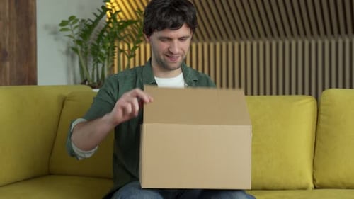 Man Opens Cardboard Box on a Yellow Couch