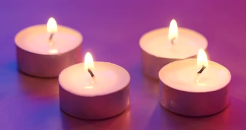 Four White Candles Glowing on Reflective Surface