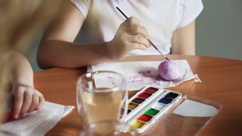Close Up of Girls Use Paintbrushes to Paint Eggs