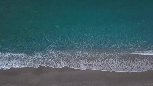 Blick von oben nach unten türkisfarbene Wellen, die am leeren Kiesstrand die Küste erreichen. Reines Meer aus der Vogelperspektive