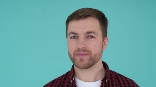 Unshaven Man in the Studio on a Turquoise Background He Looks at the Camera and Laughs