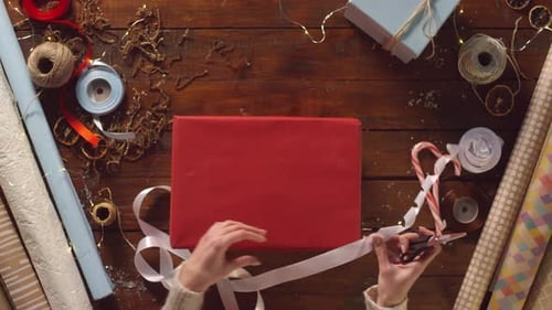 Person Wrapping Red Gift with White Ribbon