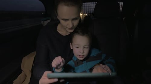 Woman and Boy with Tablet in Car at Night