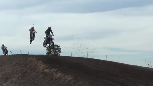Dirtbikes Jump Over Hill in Rural Area