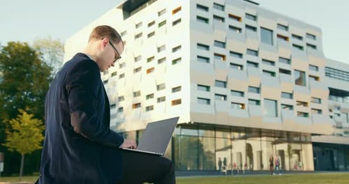 Ein Geschäftsmann sitzt auf dem Hof und arbeitet an einem Laptop