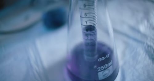 Wissenschaftler entnimmt in einem Labor eine lila Flüssigkeit aus einer konischen Flasche und verfolgt den Schuss
