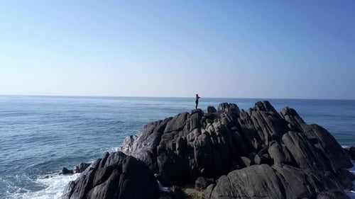 Lady Silhouette Meditates on Grey Rocky Cliff Top at Ocean