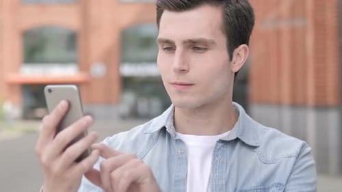 Young Adult Man Using Smartphone in Urban Setting