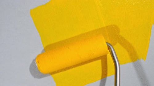 Yellow Paint Roller Applying Paint to Gray Wall