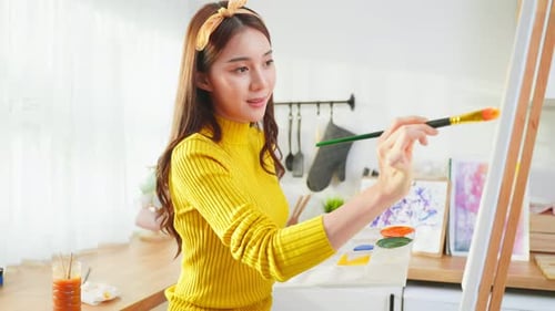 Asian young talented woman artist coloring on painting board in house.