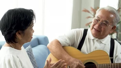 Elderly Man Playing Guitar for Woman Indoors