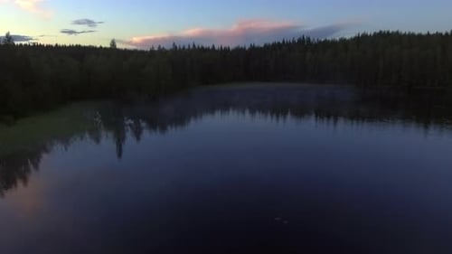 Aerial video of a remote misty forest lake by dusk in borealis wilderness.