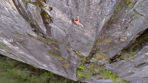 Aerial Of Experienced Rock Climber At Dangerous Heights On Mountain Cliff Above Forest