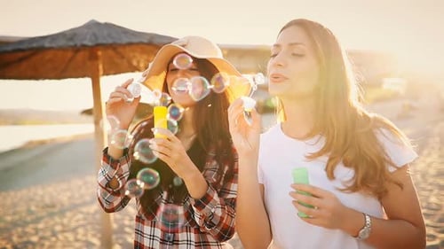 Two Friends Blowing Bubbles at the Beach at Sunset