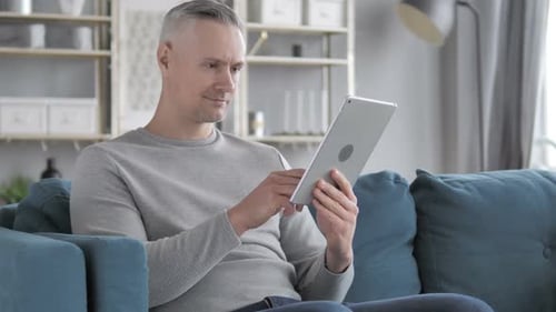 Mann mit grauen Haaren surft auf Tablet im Internet, während er auf der Couch