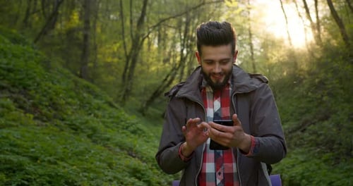 The Guy Is Looking at the Maps on the Smartphone and Goes Through the Forest