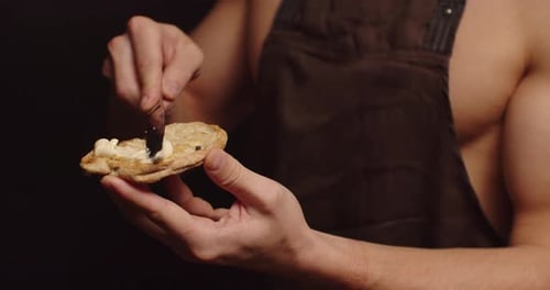 Man Spreads Cream on Bread Slice With Knife