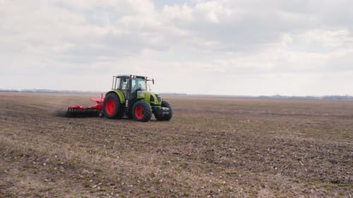 Tracteur travaillant dans un champ au premier plan d'une terre non cultivée destinée à l'ensemencement