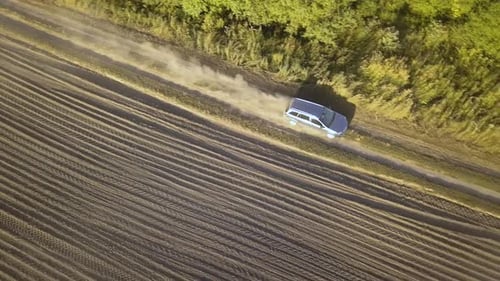 Top down aerial view of fast driving car on dirt road leaving cloud of dust behind.