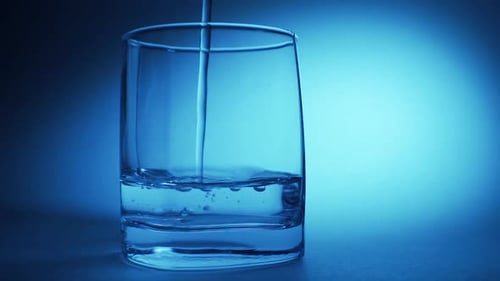 Pure Clear Water Is Poured Into a Glass on a Blue Background.