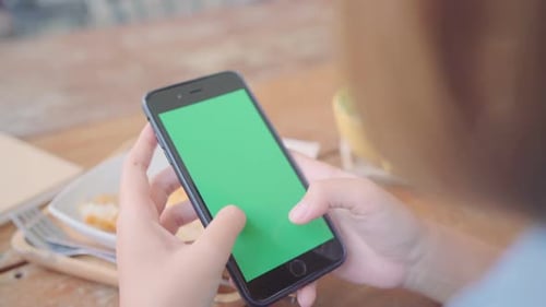 Young asian woman using black mobile phone device with green screen.