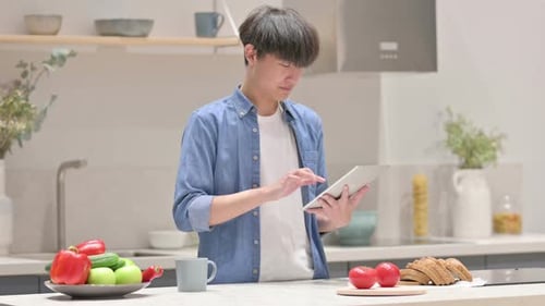 Junger asiatischer Mann benutzt Tablet, während er in der Küche steht