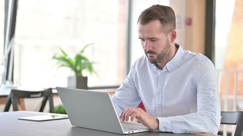 Young Man with Laptop Doing Thumbs Up in Office